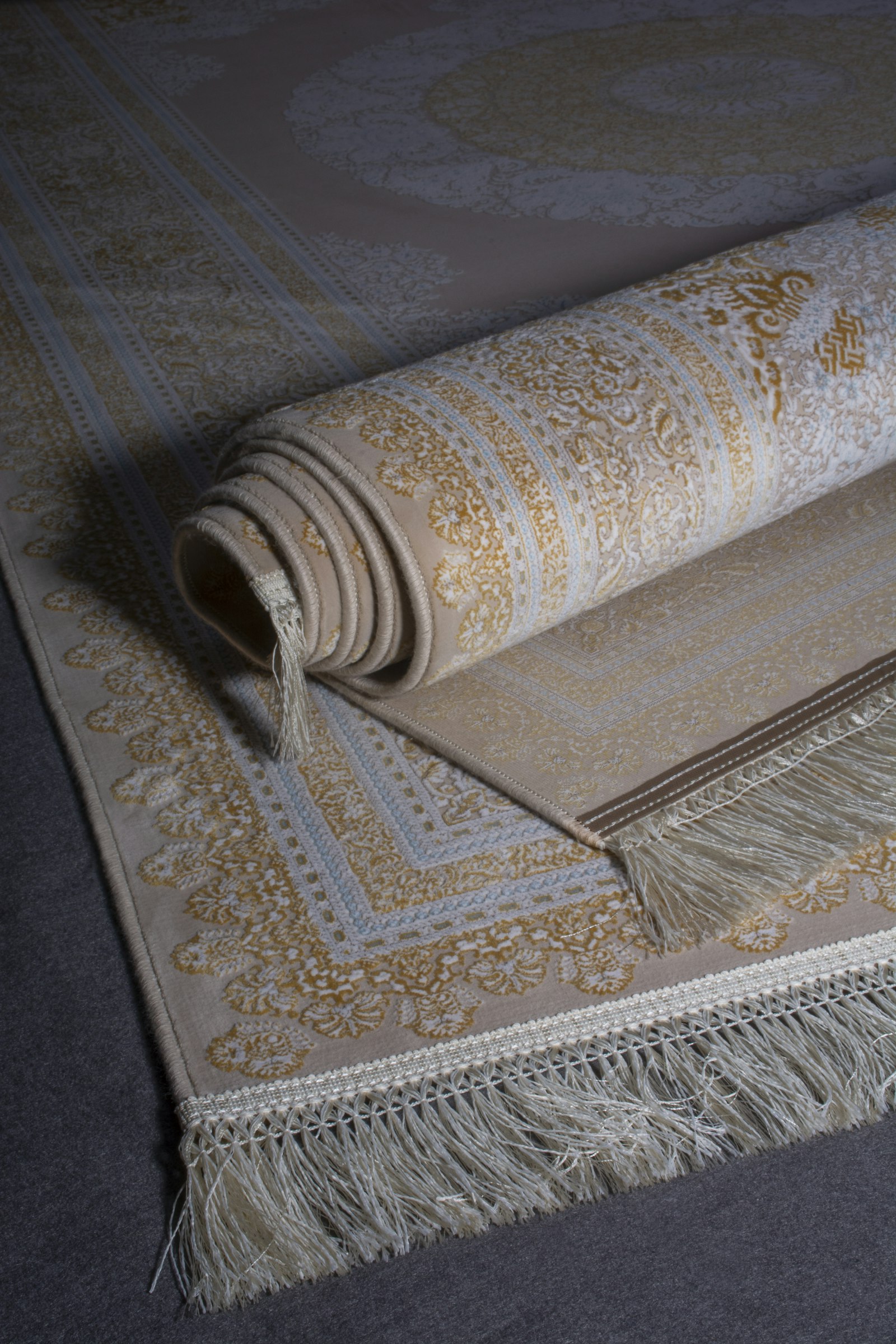 A hand-knotted carpet unrolled on a dark wood floor showing the pattern and tasseled fringe