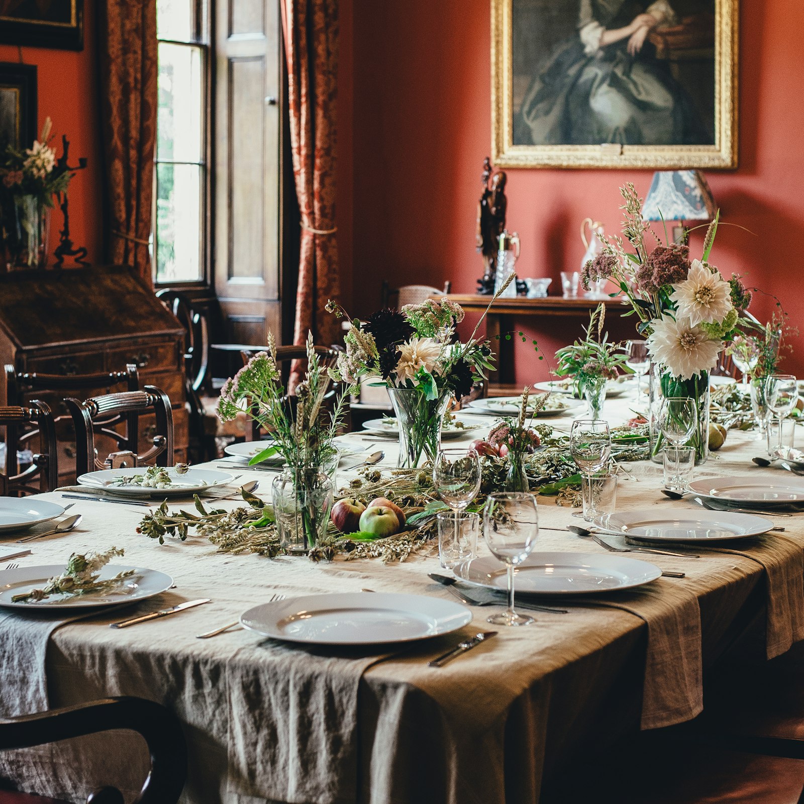 Long dining table laid with linen, wildflower vases and place settings against terracotta walls